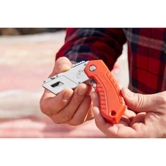 Stanley 0-10-243 folding utility knife with orange handle shown in hand outdoors.