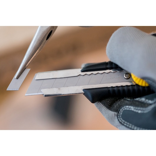 STANLEY 0-10-418 snap-off utility knife held by gloved hand, close-up of blade segment being removed.