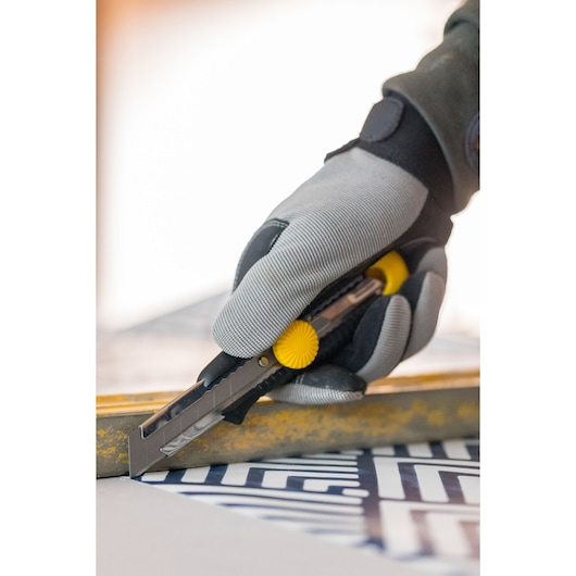 STANLEY 0-10-418 utility knife with yellow knob held by gloved hand cutting patterned material, close-up.