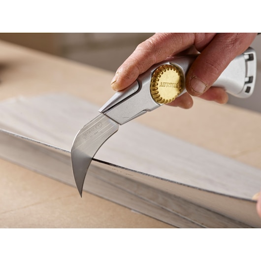 STANLEY 0-11-980 hooked blade utility knife cutting metal sheet, close-up photography.