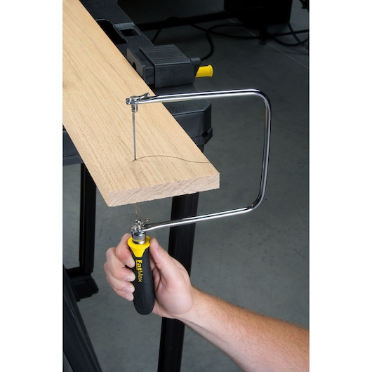 Photo of STANLEY 0-15-106 coping saw in use cutting a curved line in a wooden board from side angle.
