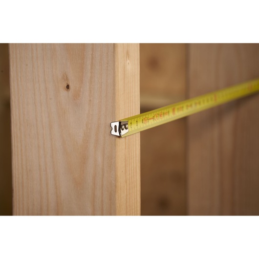 STANLEY 0-30-487 tape measure extended against wooden beam, side view, measuring distance.