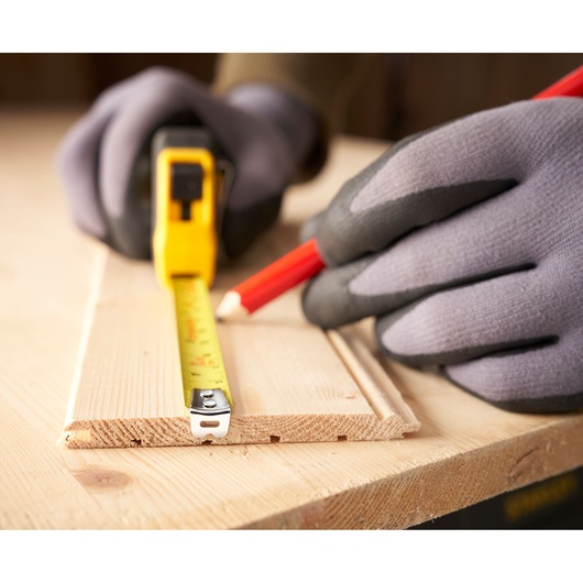 STANLEY 0-30-686 tape measure held with gloved hands, marking wood with pencil, photography close-up.