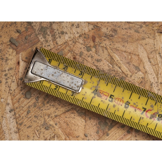 STANLEY 0-33-532 yellow tape measure with metal hook, close-up on dirty plywood.