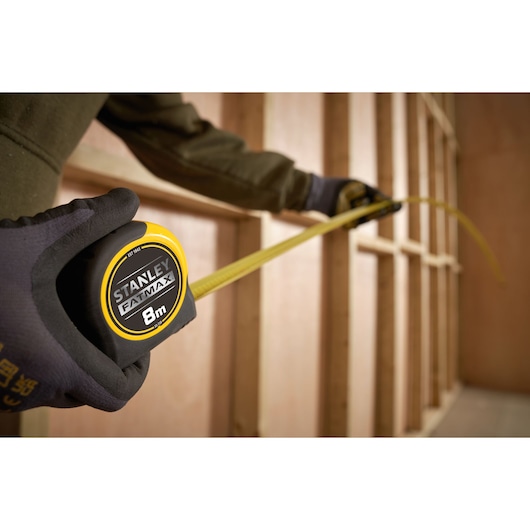 STANLEY FATMAX 8m tape measure SKU 0-33-728 being used to measure wooden studs, perspective close-up.