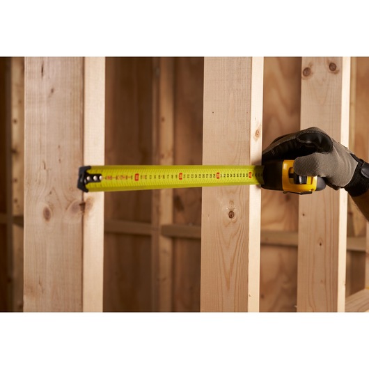 Photo of STANLEY 0-33-811 tape measure extended against wooden beams, held by gloved hand.