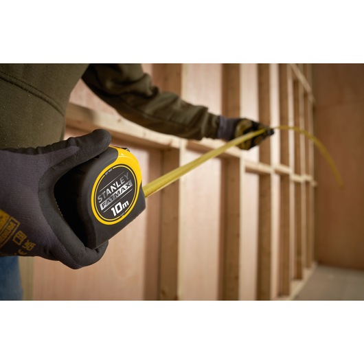 Photo of STANLEY 0-33-811 tape measure being used for measuring wooden framing, close-up of gloved hand holding the tool.