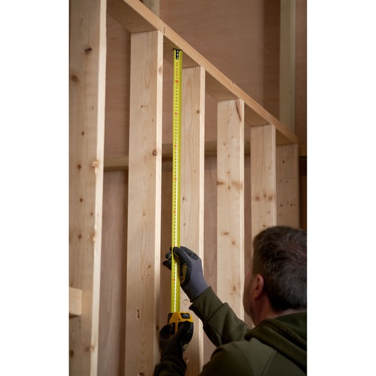 STANLEY 0-33-811 tape measure measuring vertical wooden stud in construction setting.