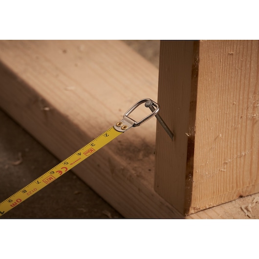 Photo of STANLEY 0-34-102 tape measure hooked on a nail in wood, close-up of measuring in progress.