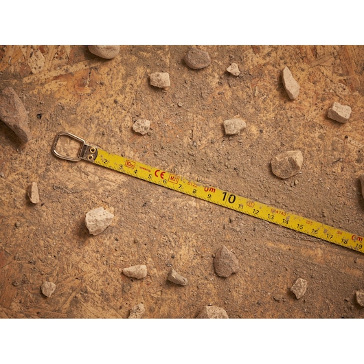 STANLEY 0-34-102 yellow tape measure on a dusty surface with scattered stones, top view.
