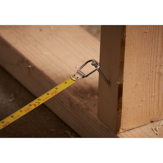 STANLEY 0-34-105 tape measure hooked on a nail in wood, close-up during carpentry work.
