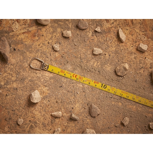 Photo of STANLEY 0-34-105 measuring tape extended on a dusty surface with scattered rocks, top view.
