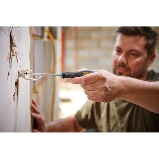 Stanley 0-65-335 screwdriver in use, close-up of hand installing wall bracket, construction setting.