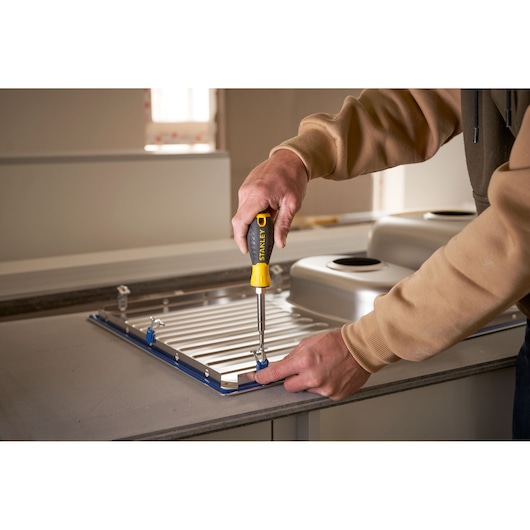 STANLEY 0-68-012 screwdriver used to install a metal sink in a kitchen, close-up from side.