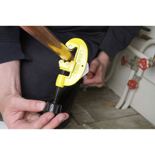STANLEY 0-70-448 pipe cutter in use, yellow body on copper pipe, hands adjusting tool, plumbing context.