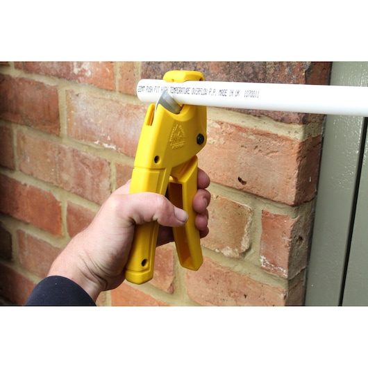 STANLEY 0-70-450 pipe cutter in yellow used to cut a white pipe near a brick wall, close-up photography.