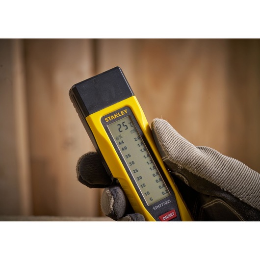 STANLEY 0-77-030 moisture meter held in gloved hand, showing digital display, close-up photography.