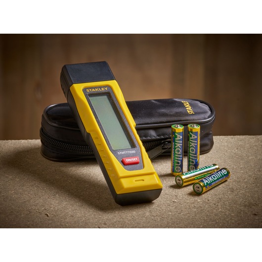 STANLEY 0-77-030 digital measuring tool with yellow and black body, soft case, and four AA batteries, front angle.