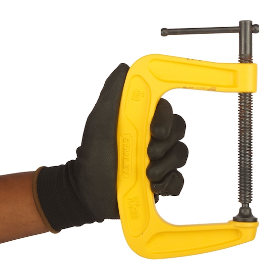 Photo of STANLEY 0-83-034 yellow C-clamp held by a gloved hand, tool photography, front angle.