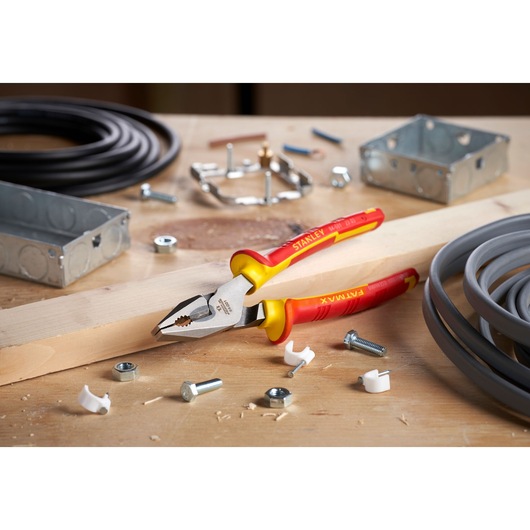 Photo of STANLEY 0-84-001 insulated combination pliers with red and yellow handles on a workbench with electrical parts.