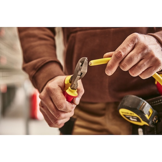 Photo of STANLEY 0-84-004 pliers cutting yellow wire, close-up view with tape measure visible.