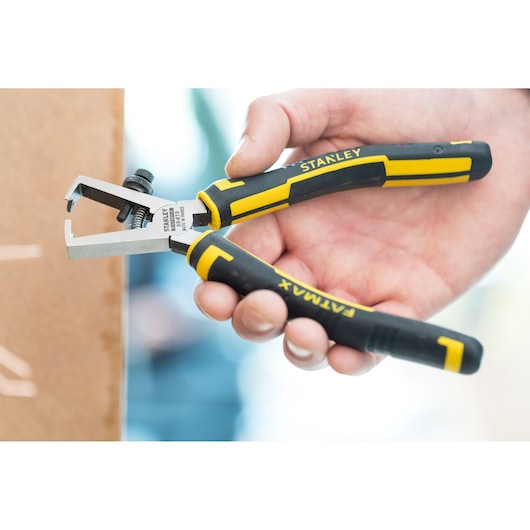 STANLEY 0-89-873 wire stripper pliers with black and yellow handle, held in hand, side view.