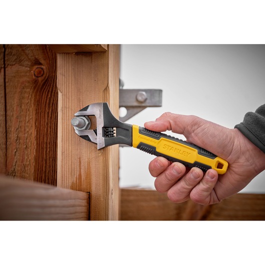 STANLEY 0-90-950 adjustable wrench with yellow and black handle tightening bolt on wooden post.
