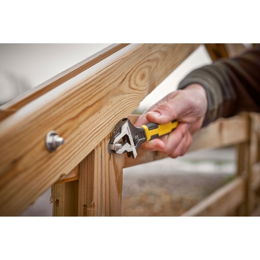 STANLEY 0-90-950 adjustable wrench with yellow handle, tightening bolt on wooden structure, close-up.