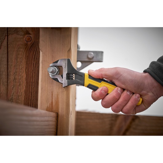 STANLEY 0-90-950 adjustable wrench with yellow grip tightening bolt on wooden beam, side angle.