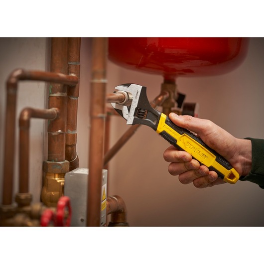 STANLEY 0-90-950 adjustable wrench being used on copper pipes, close-up, product in hand.