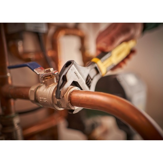 STANLEY 0-90-950 adjustable wrench gripping a brass valve on copper pipes, close-up photography.