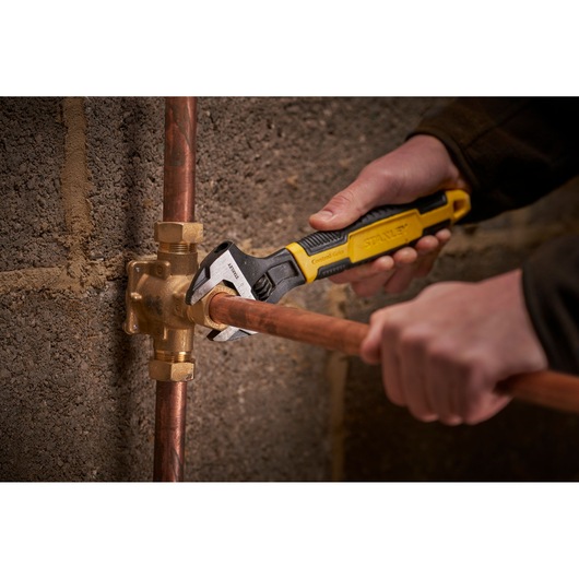 STANLEY 0-90-950 adjustable wrench used on copper plumbing pipes, close-up in a workshop setting.