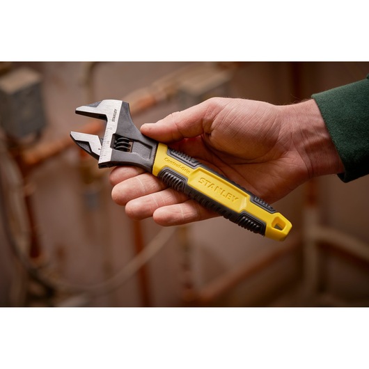 STANLEY 0-90-950 adjustable wrench with yellow and black ControlGrip handle shown in hand, plumbing background.