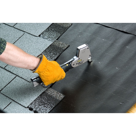 Photo of STANLEY 0-PHT350 hammer tacker in use, fastening black material on a roof with shingles visible.