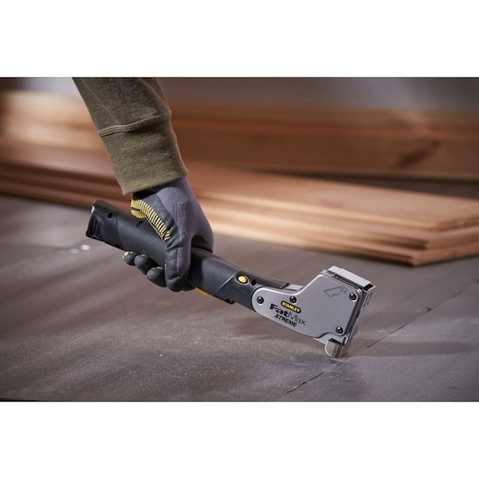 Photo of STANLEY 0-PHT350 staple gun tool held by gloved hand, used on flooring during installation.