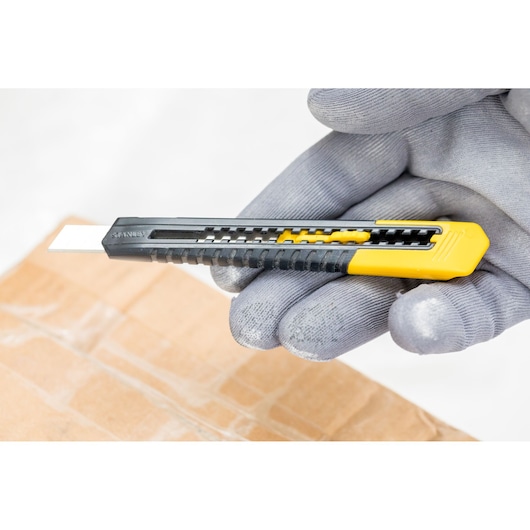 STANLEY 1-10-150 utility knife with yellow and black handle held in gloved hand, cutting cardboard.