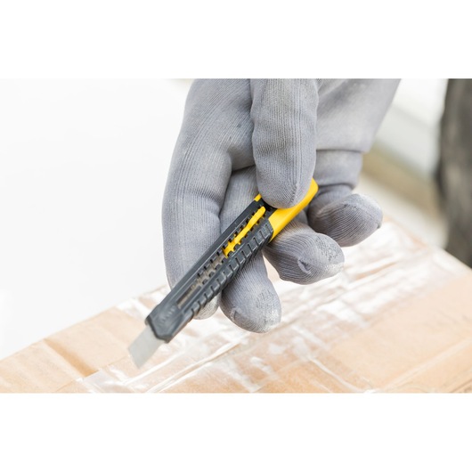 Photo of STANLEY 1-10-150 utility knife in a gloved hand cutting cardboard, close-up angle.