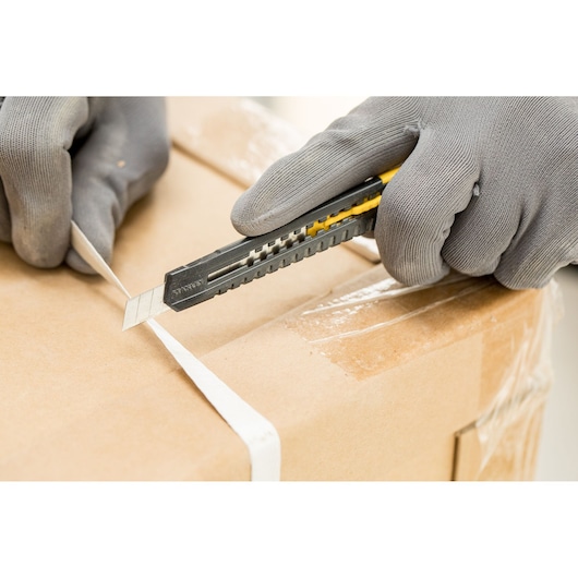 STANLEY 1-10-150 utility knife cutting packing strap on a cardboard box, close-up photography.