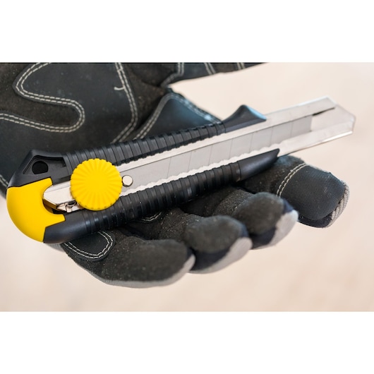 STANLEY 1-10-418 utility knife with yellow knob held in gloved hand, photography close-up angle.