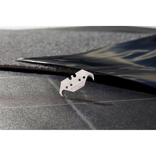STANLEY 1-11-802 hook utility blade shown cutting black material, close-up photography.