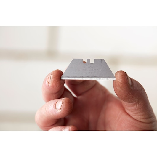 STANLEY 1-11-911 utility blade held between fingers, close-up view, silver color, sharp edge visible.