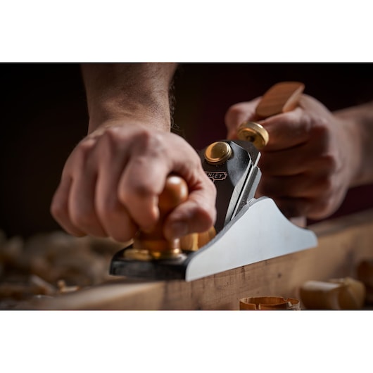 Photo of STANLEY 1-12-136 hand plane in use, close-up showing wooden handles and metal body on wood.