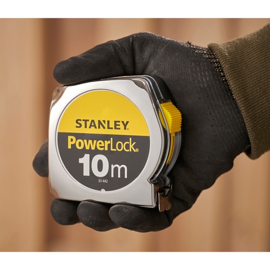 STANLEY 1-33-442 PowerLock 10m tape measure held in a gloved hand, close-up photography.