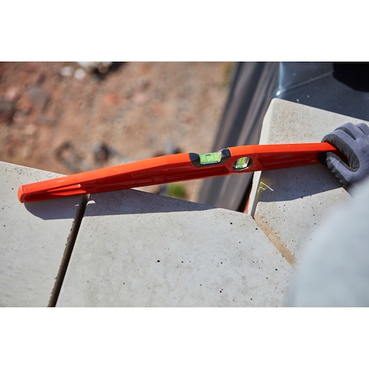 STANLEY 1-42-314 red spirit level in use on concrete tiles, close-up outdoor scene, product photography.