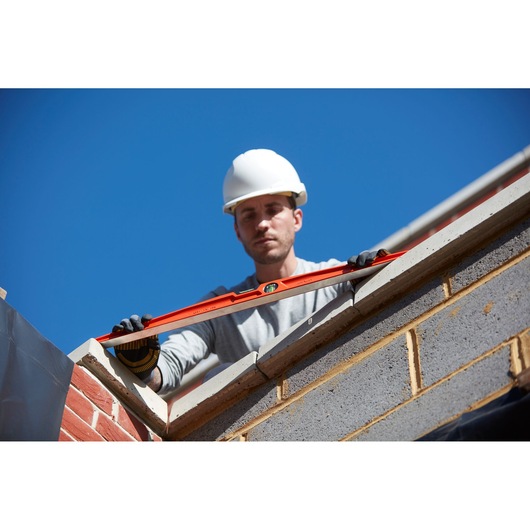 STANLEY 1-42-315 spirit level held by gloved worker on brick wall, outdoor construction scene.