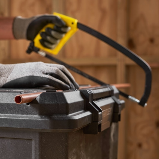 STANLEY 1-70-316 photography of gloved hands using hacksaw to cut copper pipe on black toolbox.