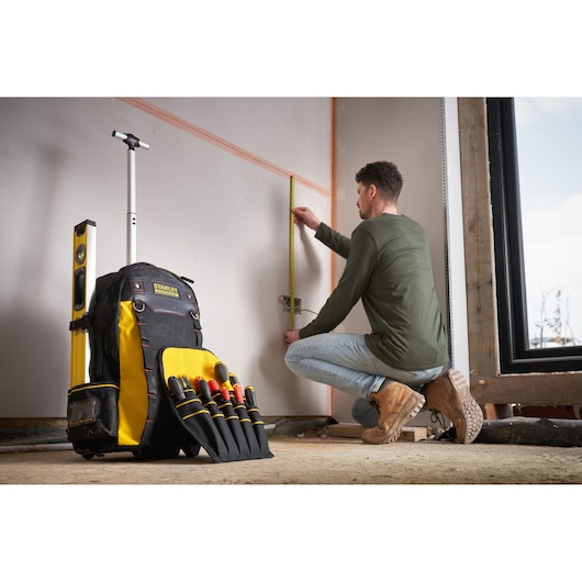 Photo of STANLEY 1-79-215 tool backpack with yellow and black color, visible hand tools, and a level, at a job site.