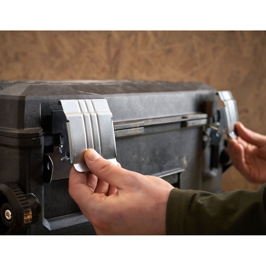 STANLEY 1-94-210 toolbox close-up, hands opening metal latches on black storage box, front angle.