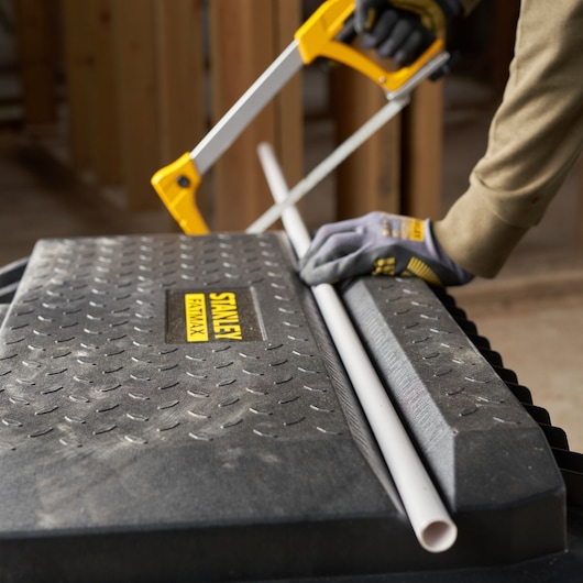Stanley 1-94-850 toolbox used as work surface, gloved hand sawing PVC pipe with Stanley saw.