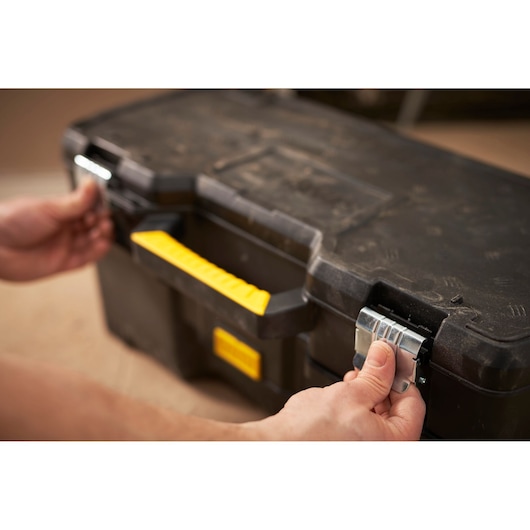 STANLEY 1-97-506 tool box with yellow handle and metal latches, hands opening front view.